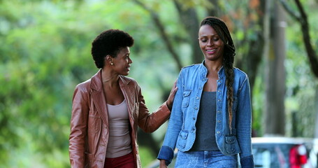 Two female friends in conversation walking outside in street talking together