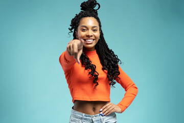 Beautiful young woman pointing finger at camera and smiling, choosing, inviting people, standing over blue background - obrazy, fototapety, plakaty