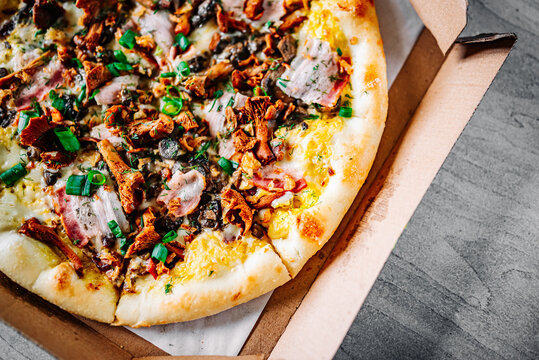 pizza with chanterelles and bacon in box on wooden background