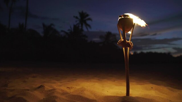 4K Torch standing upright in sand with flames flickering under blowing wind. Uninhabited island, relaxation, tropical beach concept.