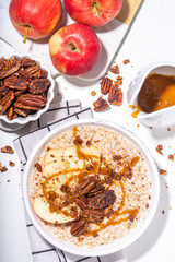 Simple autumn traditional American breakfast. Ready to eat apple pie oatmeal porridge with apples, pecans and caramel on white table background copy space