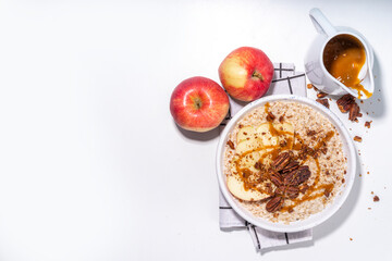 Simple autumn traditional American breakfast. Ready to eat apple pie oatmeal porridge with apples, pecans and caramel on white table background copy space
