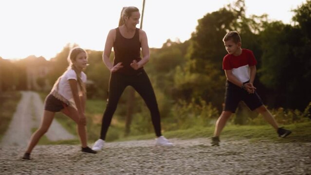 Brother and sister do stretching exercises with their mother in nature in the countryside