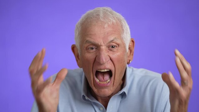 Closeup of frustrated irritated sad angry elderly gray-haired man 70s in blue shirt yelling scream isolated on plain light purple background studio portrait