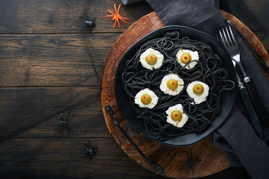Halloween party Italian black pasta decorated horror  olives like eyes on black plate on old dark table background. Monster face from pasta. Halloween decorations and Halloween food concept. Mock up.
