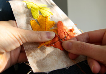 Close-up of a woman's hands sewing to produce applique work of autumn leaves.