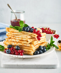 Pancakes. Stack of crepes or thin pancakes with berries, blueberries, red currants, raspberries and honey for breakfast. Homemade breakfast. Copy space. Selective focus.