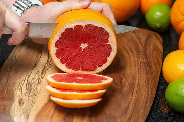 Women's hands cut juicy grapefruit into thin slices on a board