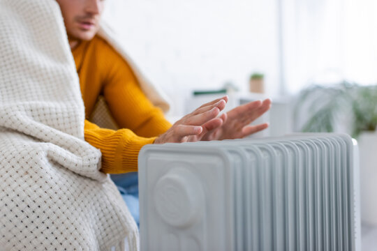 partial view of young man covered in blanket sitting on sofa and warming up near radiator heater.