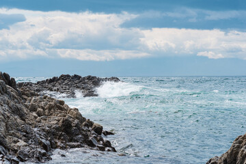 Fototapeta na wymiar coastal rocks, consisting of columnar basalt, among the sea surf, Cape Stolyuchy on the island of Kunashir