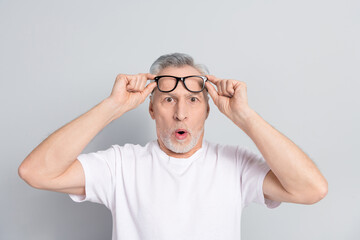 Portrait of impressed aged person hands touch eyeglasses stare isolated on grey color background