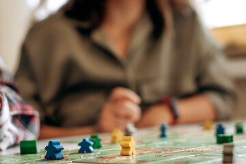 Field of tabletop game with gaming pieces in focus and blurred players on the background.Time together.Stay home,board games concept.Selective focus,close up.