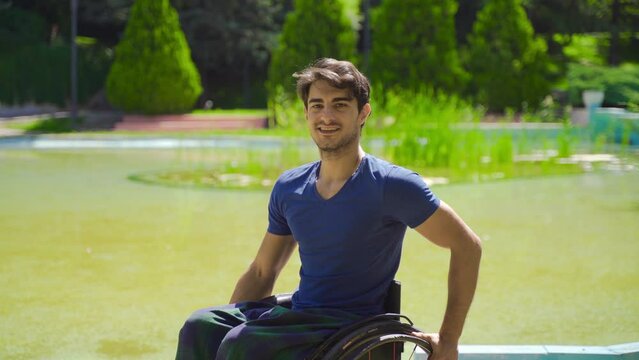 Young disabled man in wheelchair smiling looking at camera outdoors.
Disabled person traveling in a wheelchair in a nature park smiling at the camera.
