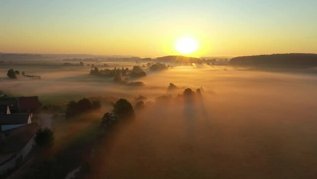 Fog morning over the plain and river floodplain of the meadow near a rural village with a house, aerial 4K view landscape. Flight over a typical German village in fog