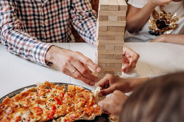 A group of multiage and multiethnic people playing jenga game on a table at home,hands close...