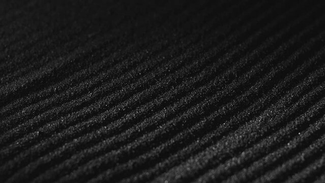 Black sand surface with paths. Abstract textured background. Dark dust falling, covering ground. Close-up