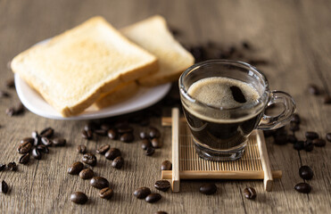 A shot glass cup of Espresso coffee with bread and coffee bean on table