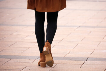 Female legs in black warm tights and brown shoes. Slim girl walking on a street, fashion in autumn...