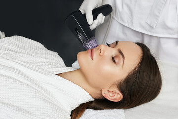 Brunette woman receiving radiofrequency lifting procedure for her face skin rejuvenation at aesthetic cosmetology clinic - 532209260