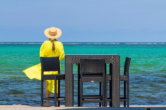 Woman in a yellow dress gazing out at turquoise waters.