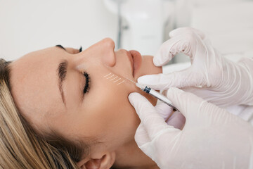 Beautician doing injection into nasolabial folds to female patient. Correction of wrinkles on woman...