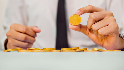 Businessman holding a coin and a pile of coins on the table.