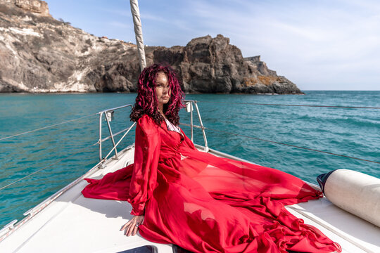 Attractive middle-aged woman in a red dress on a yacht on a summer day. Luxury summer adventure, outdoor activities.
