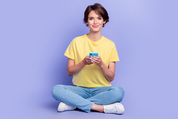 Full length photo of charming nice person sit floor hold use telephone isolated on violet color background