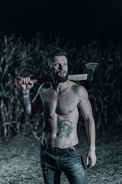 Scary man with ax stands in corn field and looks into camera at night. Halloween concept