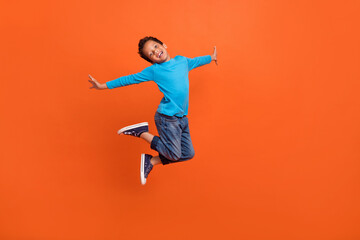 Obraz na płótnie Canvas Full length photo of adorable little pupil boy jumping school shopping poster wear trendy blue clothes isolated on orange color background