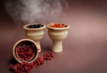 Three hookah bowls with aromatic tobacco with smoke on a brown table with smoking accessories. Hookah smoking in a hookah lounge. Red, yellow, black hookah tobacco