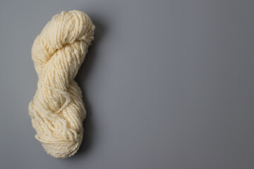 knitting and wool craft background - lovely cream and white natural coloured skein of art yarn pure wool on grey background with copy space 