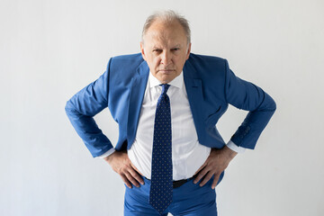 Portrait of frowning mature businessman looking at camera. Senior manager wearing formalwear standing with hands on hips against white background. Angry boss concept - Powered by Adobe