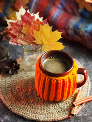 A mug of hot coffee or chocolate in a knitted orange jelly. Maple autumn leaves and a knitted warm...