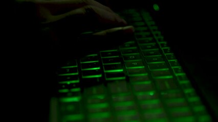 person typing on a laptop with green backlight keyboard in the dark