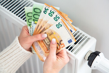 Radiator and euro money banknotes in woman hands. Expensive gas heating cost. High home heating bills in Europe.