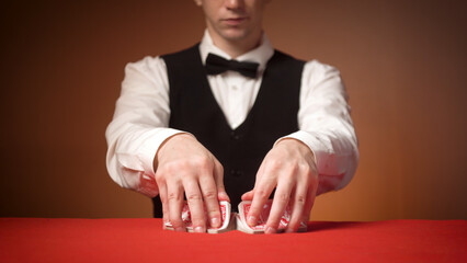 young male croupier shuffles cards before the start of the game. red table.