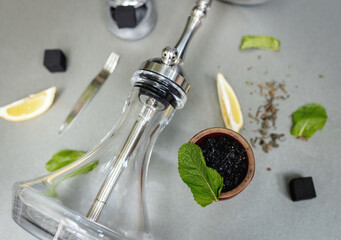 Hookah bowl with aromatic tobacco with lemon and mint on gray table with smoking accessories. Hookah smoking in a hookah lounge. Steel hookah, tongs, tea and coconut charcoal
