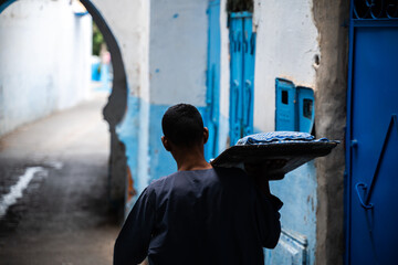 Hombre musulman portando comida por callejon con arcos azules y blanco.