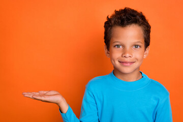 Photo portrait of adorable small pupil boy palm hold copyspace cheerful model dressed stylish blue look isolated on orange color background