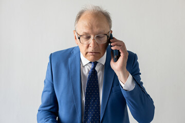 Portrait of serious mature businessman talking on mobile phone to client. Senior manager wearing formalwear and eyeglasses communicating via smartphone. Mobile communication concept