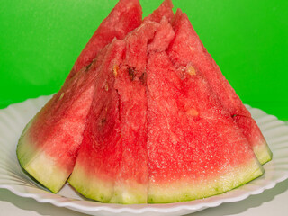 Melon culture. An annual herbaceous plant. Sliced watermelon on a white plate on a green background. Red pieces of ripe watermelon in autumn.