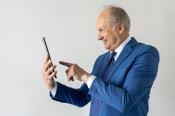 Side view of cheerful mature businessman using digital tablet. Senior manager wearing formalwear watching newsletter on touchpad and smiling against white background. Wireless technology concept