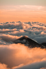 Pico de montaña apareciendo sobre mar de nubes.  - obrazy, fototapety, plakaty