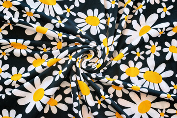 Daisies printed on fabric with black background. Wrinkled fabric with spiral effect in the center. Silk effect textile material.
