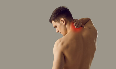 Rear view of naked young man on grey studio background ouch neck suffer from ache. Pain in upper spine area. Guy struggle with backache have inflammation or spasm. Health problem concept. - obrazy, fototapety, plakaty
