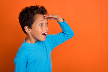 Photo of astonished cheerful boy interested look empty space cool proposition wear stylish blue jumper isolated on orange color background