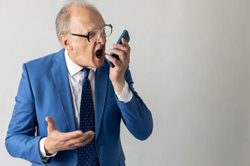 Portrait of frustrated mature businessman shouting in smartphone. Senior manager wearing formalwear...