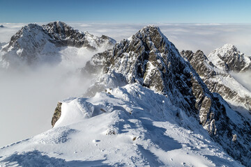 View of dramatic, rocky, snowy mountain range peaks with mist and clouds, Lomnicky Stit, High Tatras, Slovakia, European alps.