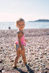 Little smiling girl in a swimsuit stands sideways on the beach. High quality photo